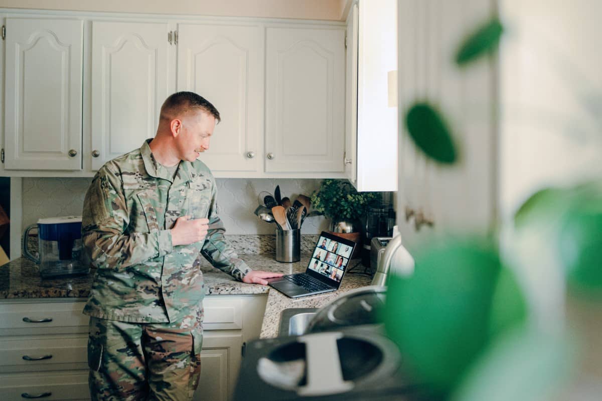 Man in military uniform reviewing content on his laptop at the kitchen counter.