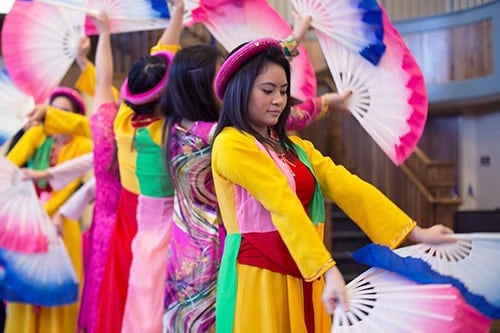 A group of women dressed in colorful outfits using large, decorative fans in a dance routine.