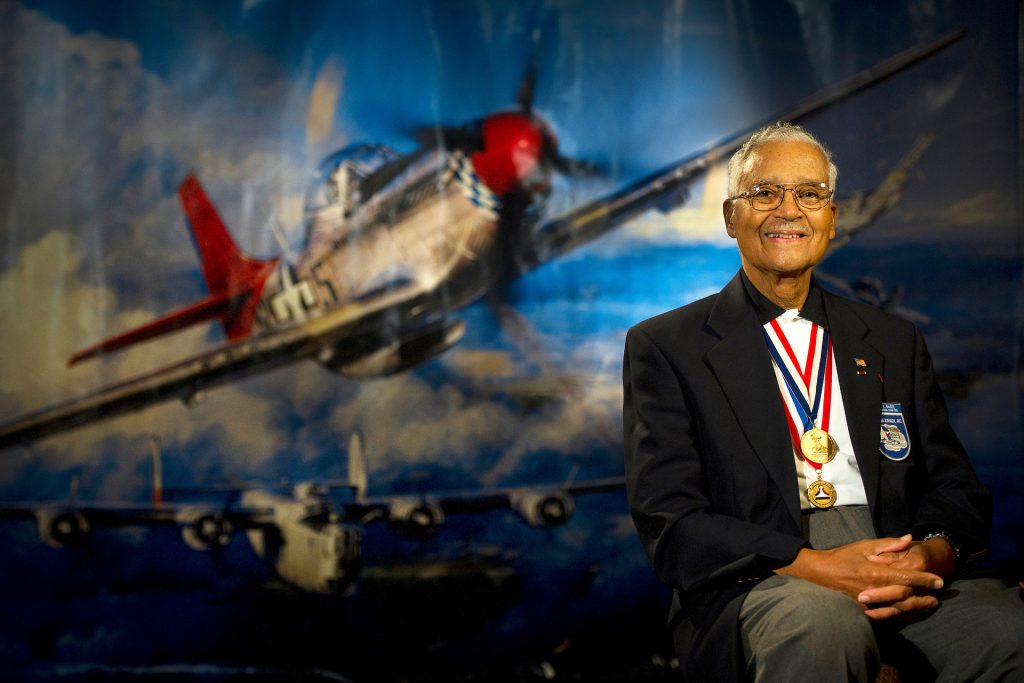 U.S. Air Force Col. (Ret.) Charles E. McGee Jr., seated, smiles for a portrait, wearing medals around his neck.