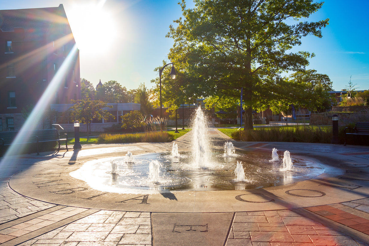 Close up view of Alumni fountain in full motion with main campus buildings in the background.