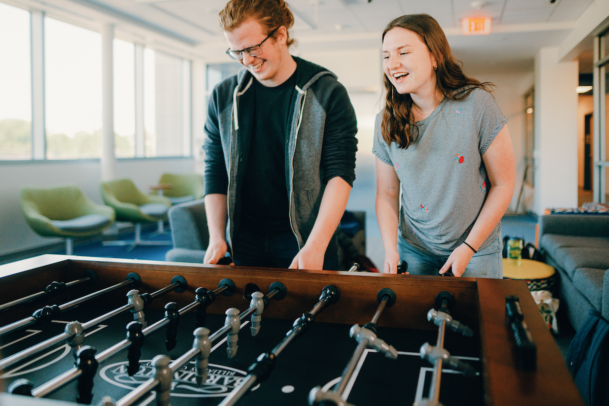 Two students laughing as they play foosball.