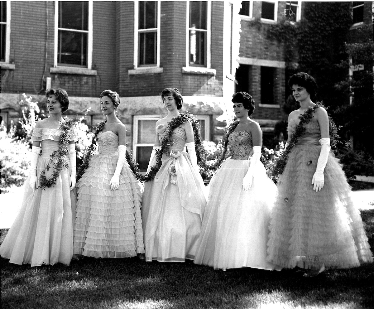 Historical image of five women standing in a semi-circle, wearing gowns with the ivy chain draped across their shoulders.