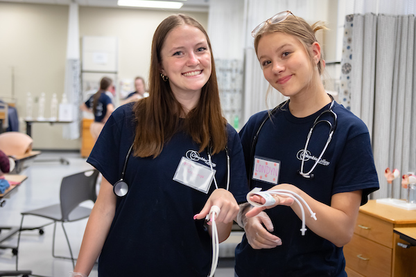 Two nursing students smile for the camera while wearing medical apparatus on their fingers.