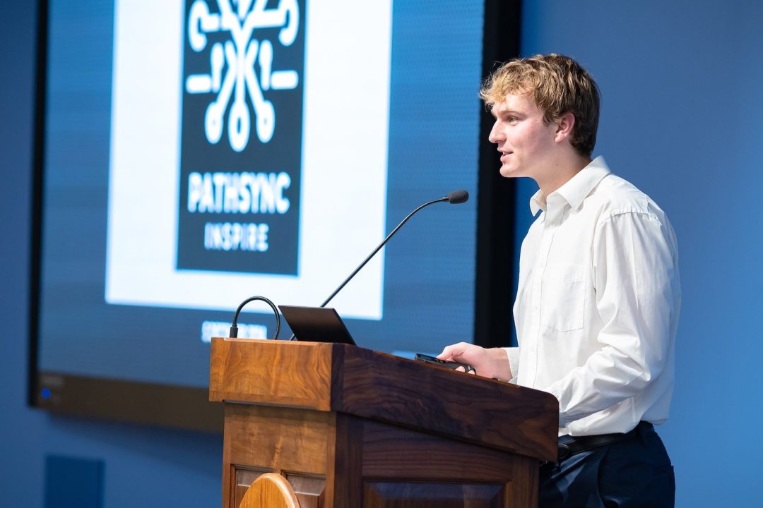 Student standing at a podium with a microphone and laptop, giving a speech.