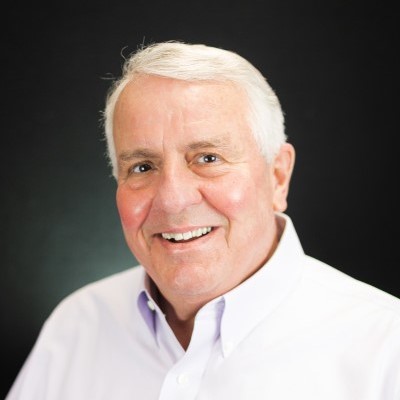 Headshot of Robert Hohenstein, in a white button up shirt, smiling at the camera a Caucasian male with white hair