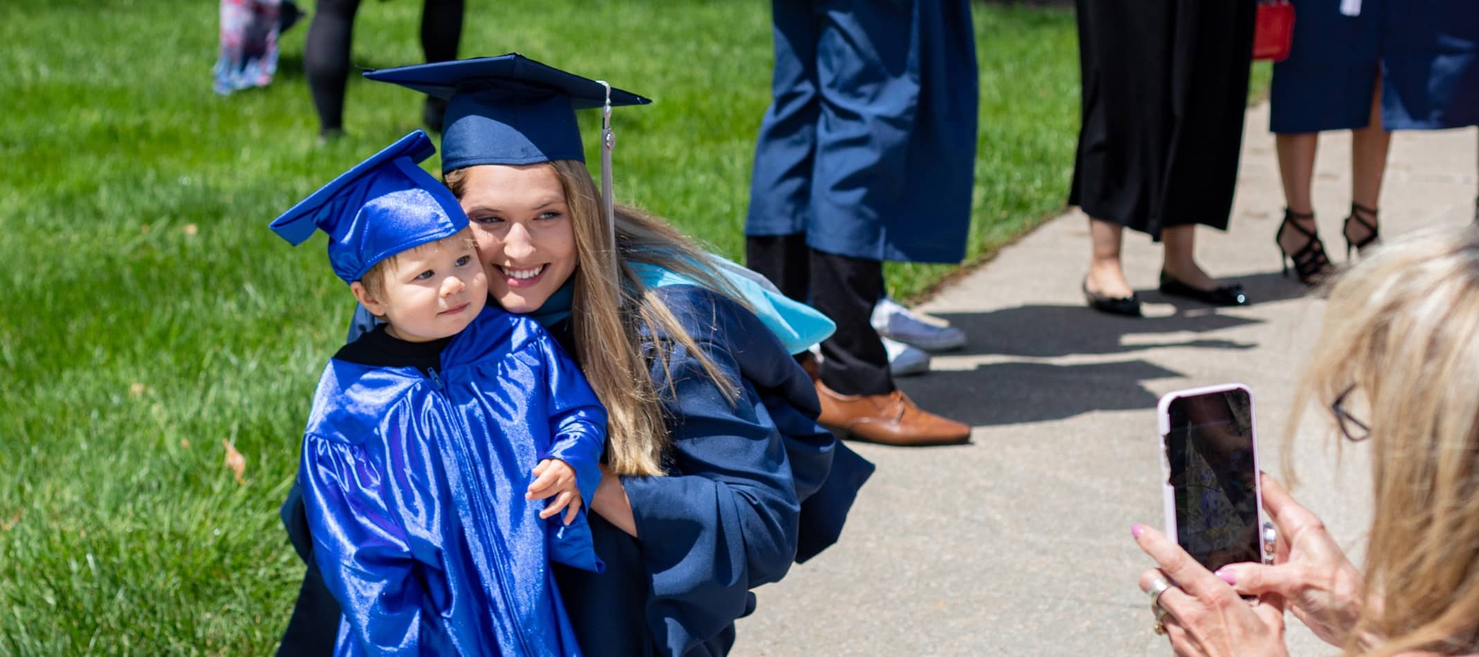 Graduate in full regalia, kneeling next to her young son - also in rull regalia - at Commencement.