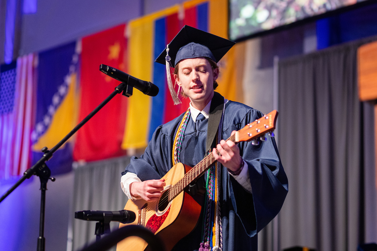 Graduate playing guitar and singing on the stage during the commencement ceremony.