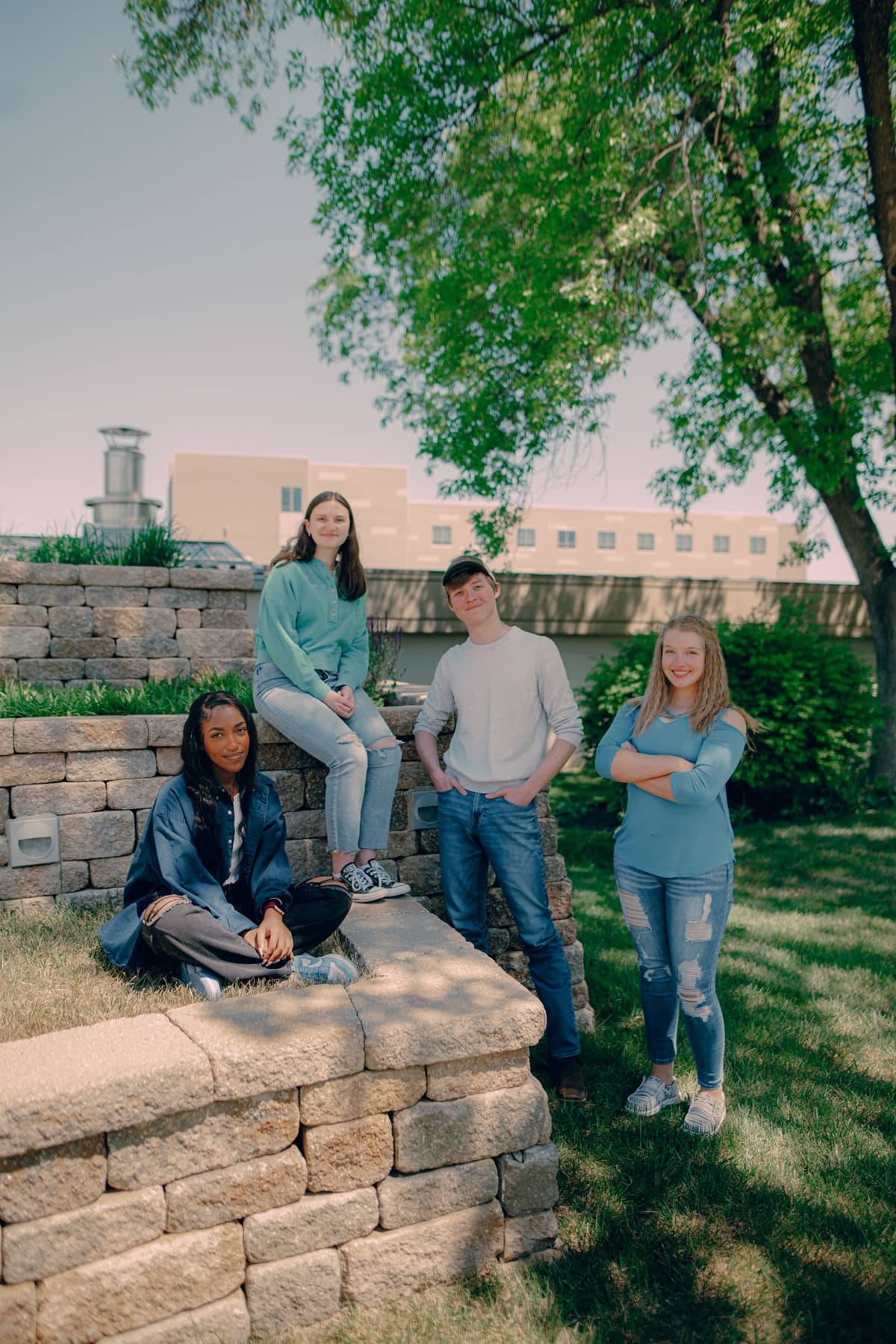 Four students, two sitting, two standing, smile for the camera on main campus.