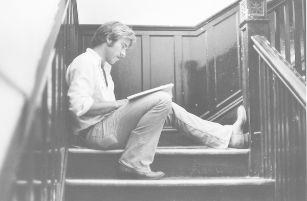 Historical image of male student sitting on the stair well while writing on a notebook.